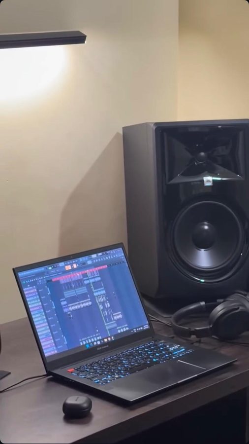 A laptop running a DAW session on a desk beside a studio monitor and headphones